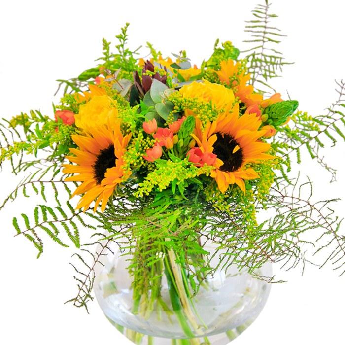 This sun-drenched bouquet is a true reflection of Chase Cross's lively character and love of nature. A gathering of show-stopping sunflowers takes centre stage, their plush, golden petals and earthy centers exuding warmth, much like the familiar welcome of the Chase Cross community. Intertwined with the sunflowers are delicate yellow garden roses, their elegantly curled petals unfolding in generous layers that reveal a hidden softness and a delicate, sweet fragrance. Sprinkled between these grand blooms are clusters of bright red hypericum berries - their glossy, berry-red skins shimmering with the promise of good cheer. The bouquet is richly layered with various shades and textures of green: trailing ferns, wispy filler flowers with miniature yellow buds, and stately, slender spikes that create a sense of depth and organic rhythm, reminiscent of a wildflower meadow along the edge of Chase Cross's green spaces. Wisps of blue-green eucalyptus enhance the arrangement with a gentle aroma and a hint of rustic allure. All elements are anchored in a clear, spherical glass vase that allows the vitality of the green stems and the clarity of fresh water to shine through. This exuberant design serves beautifully as a centrepiece for celebrations or as an uplifting gift delivered throughout Chase Cross, honouring the area's closeness to nature and its tradition of heartfelt gatherings.