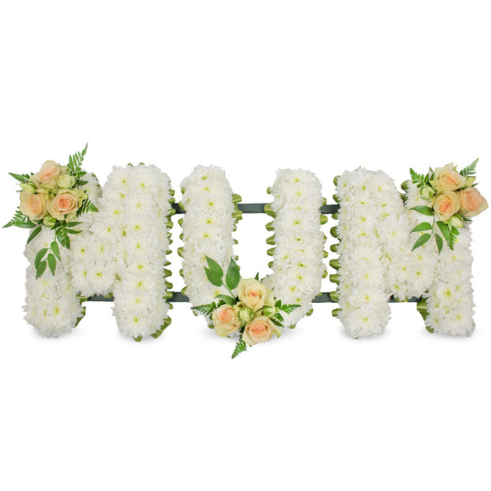 The photograph shows a classic "MOM" funeral flower tribute, arranged in a long, horizontal line and set against a stark white background that brings its textures and colours into sharp focus. The three letters, all in clear, block capitals, are constructed on a dark supporting frame that peeks out only subtly at the edges, allowing the flowers to dominate the eye. Each letter is densely covered in small, pure white blooms, likely spray chrysanthemums, which are placed in such close proximity that no gaps of green or framework are visible from above. This dense layering creates a plush, cushioned surface, with the individual petals forming intricate patterns that suggest softness and care. Tracing the outer boundary of the letters, a narrow edge of deep green floral ribbon and foliage provides both definition and contrast, outlining the shapes so they stand out clearly when viewed from a distance at a chapel in Chase Cross or during a procession through nearby Romford streets. Three clusters of soft peach and apricot roses, each enriched with buds and leafy greens, are set into the design as gentle focal points. One nestles into the upper left of the first "M", a second balances the lower centre of the "O", and a third graces the upper right of the final "M", creating a visual rhythm along the tribute. The roses offer a warm, tender counterpoint to the pristine white base, and their accompanying greenery-feathery ferns and broader, glossy leaves-adds depth and a subtle sense of movement. Crafted with the sensitivity of an experienced local florist, this "MOM" tribute feels both traditional and deeply personal, ideal for families in Chase Cross and surrounding areas wanting to express undying love, respect, and thanks in a simple, beautiful way.