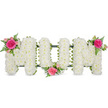 A beautifully composed floral tribute spelling the word "MOM" stands out clearly against a plain white background, the design reminiscent of the bespoke sympathy tributes often delivered across Chase Cross and Collier Row. The three bold capital letters are constructed on a sturdy green frame that can be glimpsed along the base, ensuring the arrangement remains secure and neatly shaped. Every surface of each letter is densely covered in small white chrysanthemums, their compact flower heads closely packed together to form a thick, cushioned texture that looks soft to the touch. The petals are a pristine white, catching the light in a way that gives the tribute a gentle, almost glowing presence, while tiny green eyes at the centres provide subtle depth and vitality. To soften the strong lines of the letters and add warmth, three decorative clusters of roses and foliage are placed at key points. On the top left of the first "M", a vivid fuchsia rose unfurls its velvety petals, surrounded by pale pink spray roses and buds that hint at loving memories and tenderness. Delicate green fern fronds extend lightly around the flowers, their finely cut leaves introducing movement and a natural, garden-like feel. Another, similar cluster rests between the lower section of the "O" and the beginning of the last "M", gently drawing focus to the middle of the tribute. A final matching grouping sits at the upper right corner of the second "M", echoing the first and creating a balanced, harmonious finish. The overall effect is of a timeless, heartfelt funeral flower arrangement, thoughtfully crafted to honour a beloved mother with serenity, respect, and deep affection from her family in the Chase Cross community.